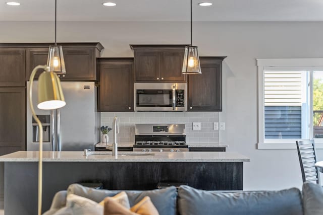 kitchen with light stone counters, dark brown cabinets, appliances with stainless steel finishes, decorative light fixtures, and backsplash