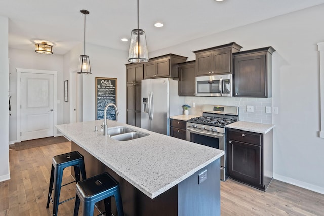 kitchen featuring a sink, stainless steel appliances, dark brown cabinets, light wood-type flooring, and backsplash