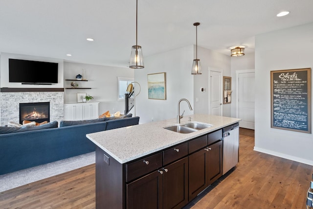 kitchen with a sink, a stone fireplace, wood finished floors, and dishwasher