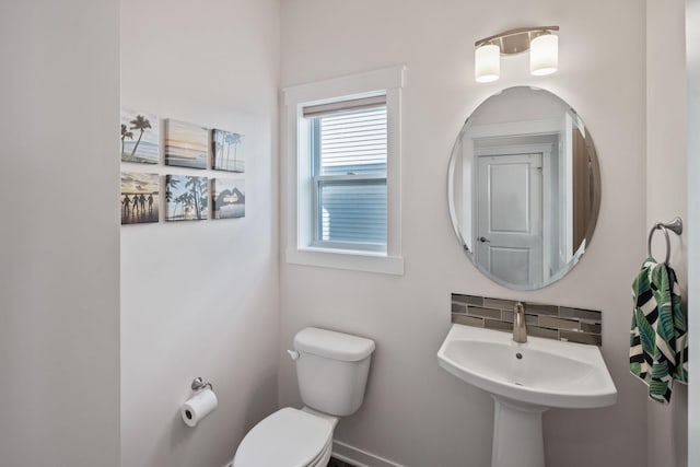 half bathroom with decorative backsplash, toilet, and a sink