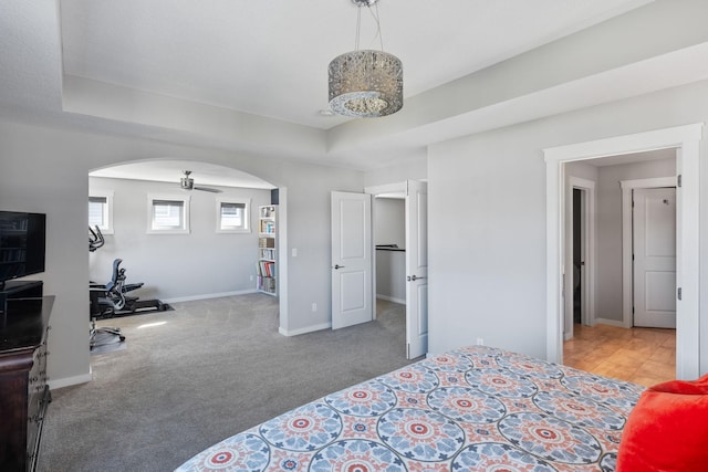 bedroom with arched walkways, carpet flooring, a raised ceiling, and baseboards