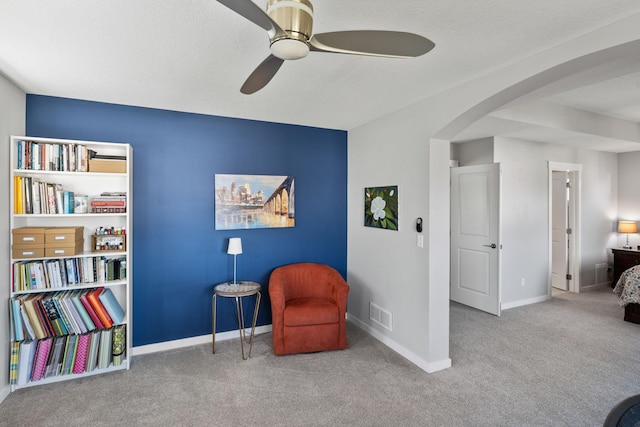 sitting room featuring carpet, visible vents, baseboards, arched walkways, and ceiling fan