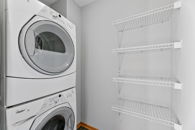 washroom with a textured ceiling, laundry area, and stacked washer / dryer