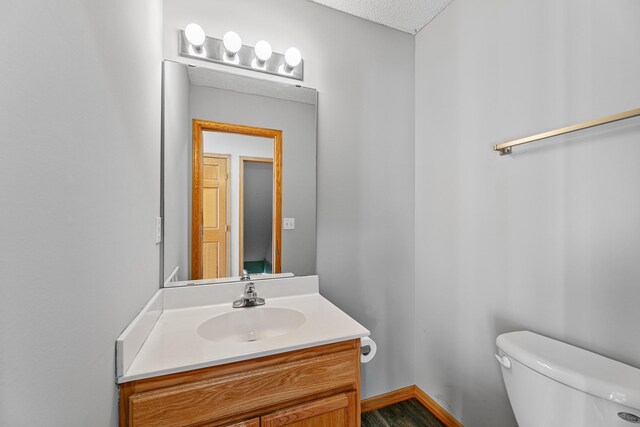 half bath featuring toilet, vanity, and baseboards