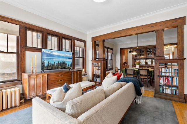 living room featuring radiator, wood finished floors, ornamental molding, and ornate columns