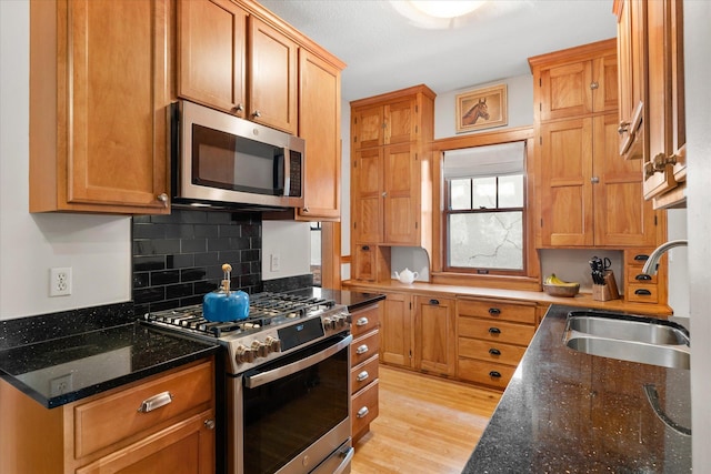 kitchen featuring dark stone countertops, light wood finished floors, a sink, appliances with stainless steel finishes, and tasteful backsplash