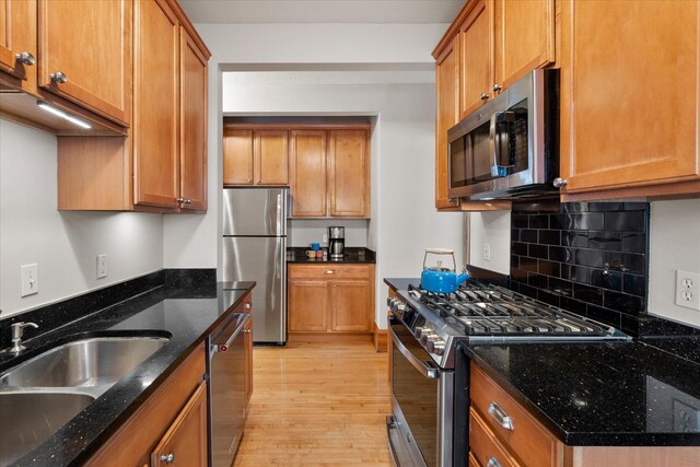 kitchen with light wood finished floors, tasteful backsplash, appliances with stainless steel finishes, brown cabinetry, and a sink