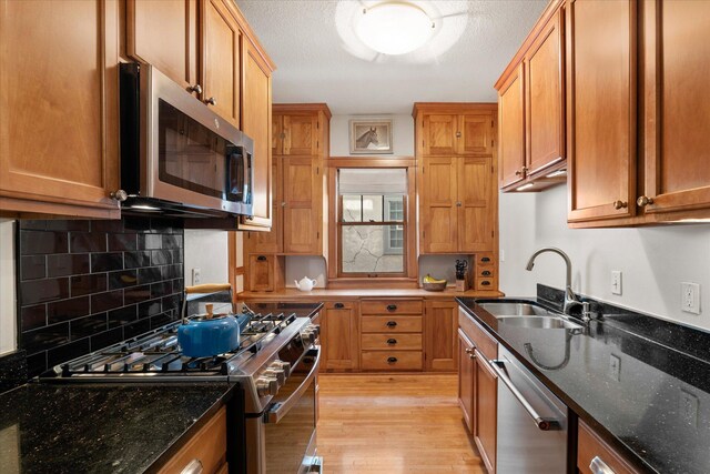 kitchen featuring dark stone countertops, light wood-type flooring, a sink, stainless steel appliances, and brown cabinets