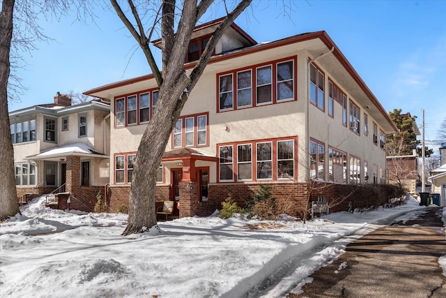 view of front of home featuring a chimney, brick siding, and stucco siding