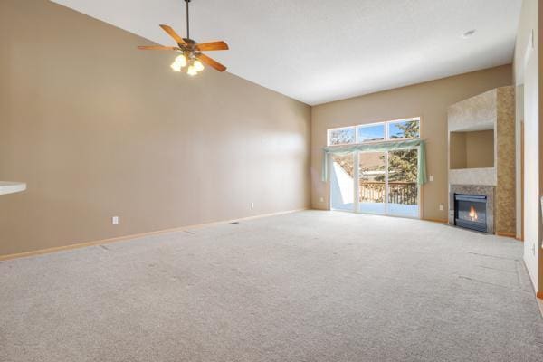 unfurnished living room with a glass covered fireplace, ceiling fan, baseboards, and carpet