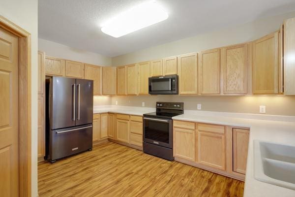 kitchen featuring light wood-type flooring, light brown cabinets, a sink, appliances with stainless steel finishes, and light countertops