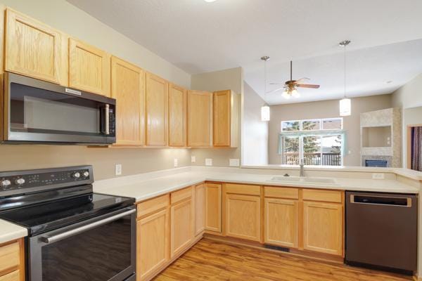 kitchen with light brown cabinets, a sink, appliances with stainless steel finishes, a peninsula, and light countertops