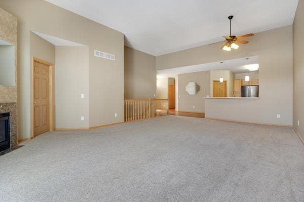 unfurnished living room with visible vents, baseboards, carpet floors, a fireplace, and a ceiling fan