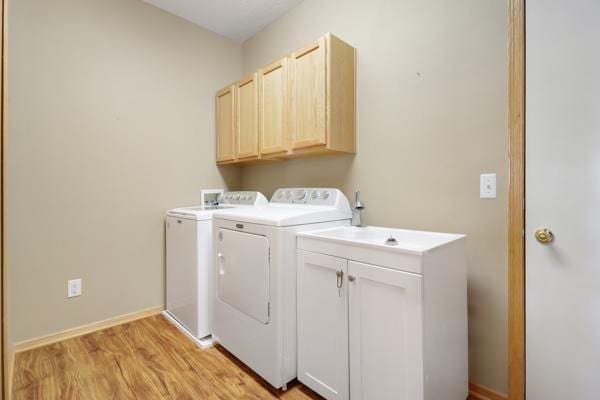 laundry area featuring light wood-style floors, cabinet space, independent washer and dryer, and baseboards