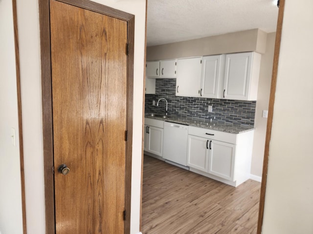 kitchen featuring tasteful backsplash, light wood-type flooring, white dishwasher, white cabinets, and a sink