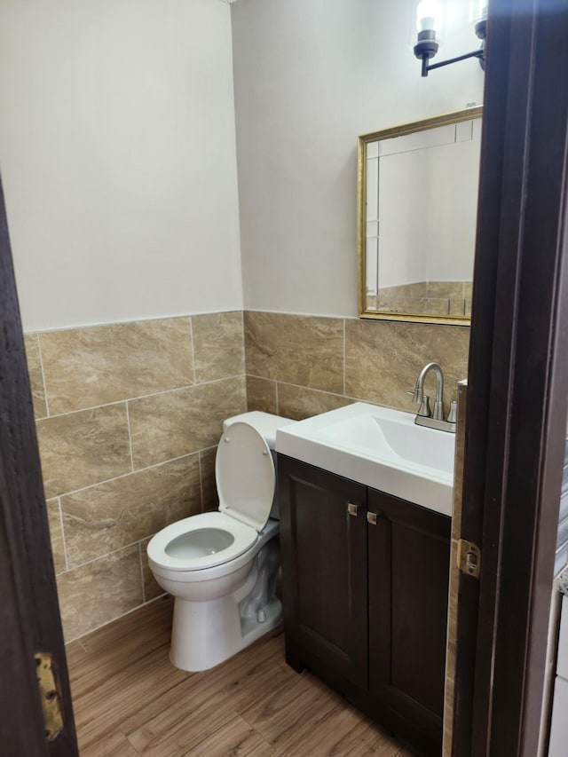 half bathroom featuring vanity, tile walls, toilet, and wood finished floors