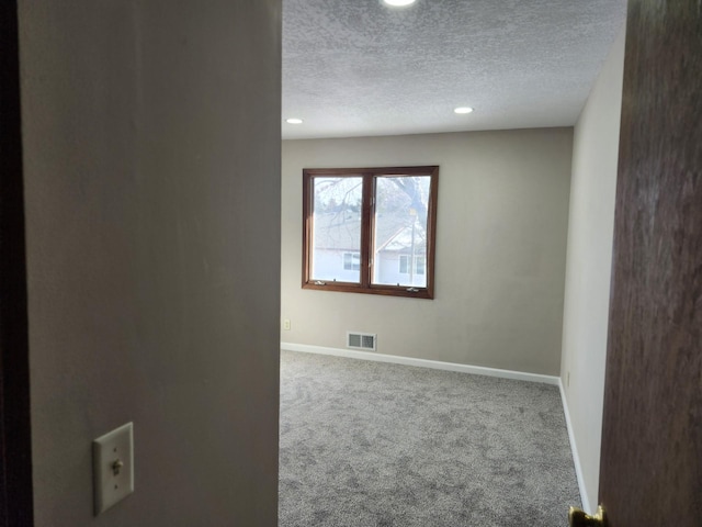 empty room featuring visible vents, baseboards, carpet, and a textured ceiling