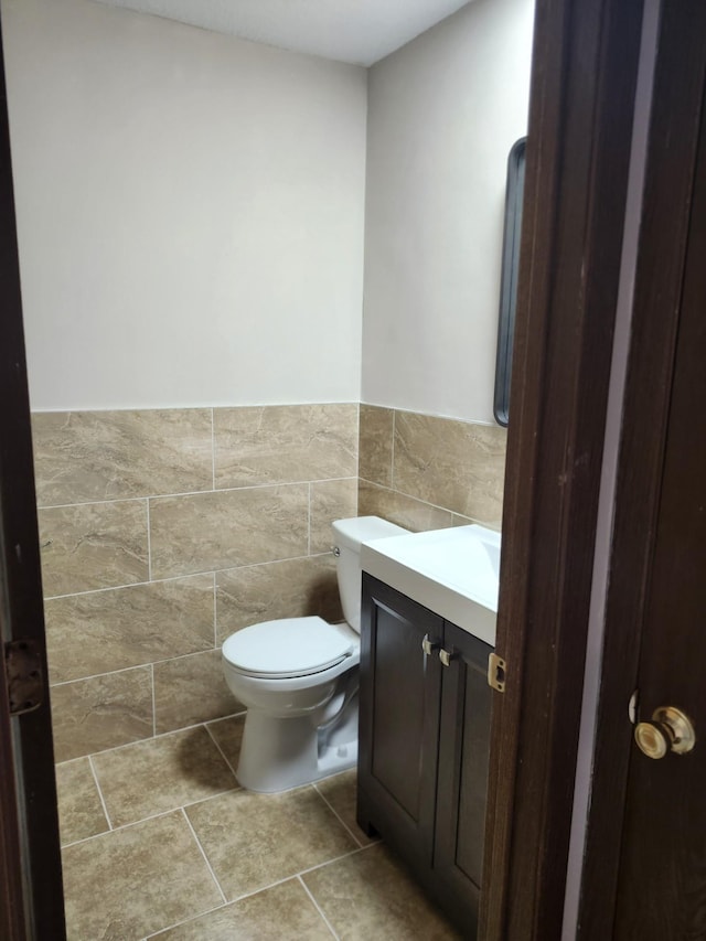 half bath featuring vanity, a wainscoted wall, tile walls, toilet, and tile patterned floors