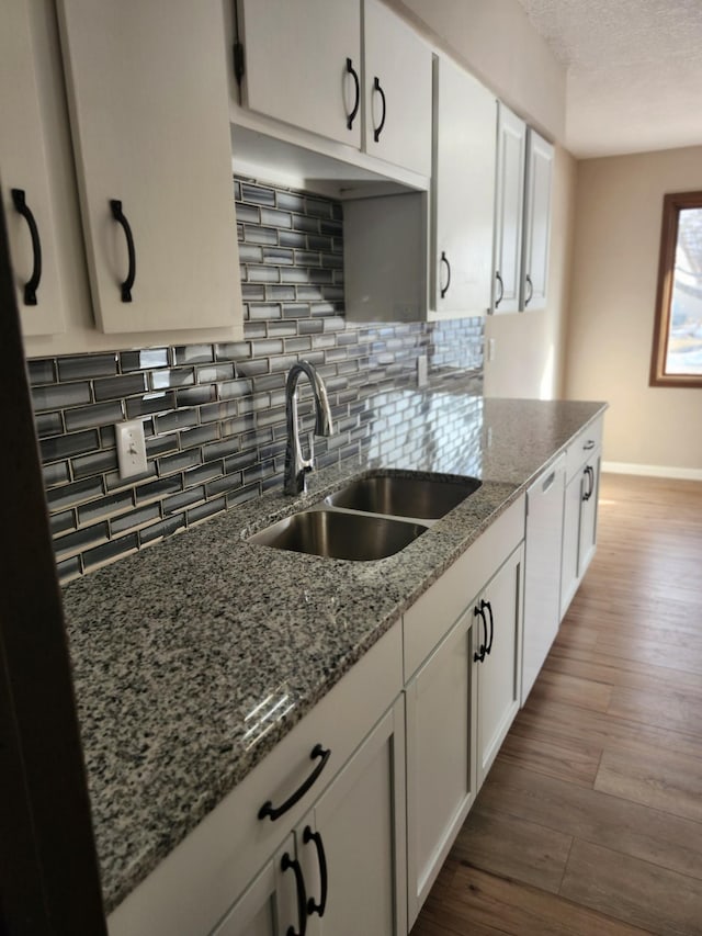 kitchen featuring wood finished floors, stone countertops, a sink, white cabinets, and tasteful backsplash