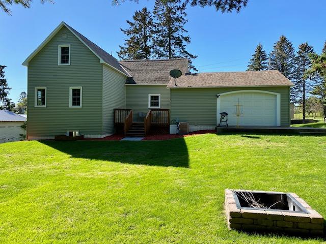 back of property featuring a yard, central AC unit, a garage, and an outdoor fire pit