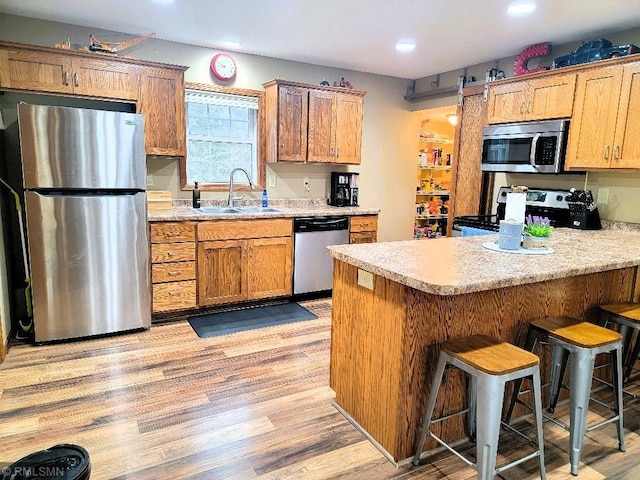 kitchen with a peninsula, a sink, light countertops, appliances with stainless steel finishes, and light wood-type flooring