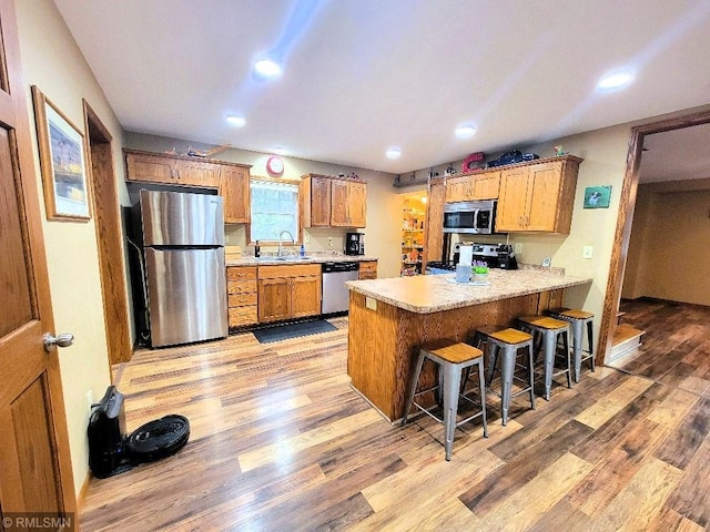 kitchen with light wood finished floors, a peninsula, a sink, light countertops, and appliances with stainless steel finishes