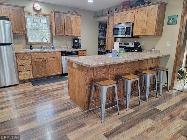 kitchen featuring a sink, stainless steel appliances, a peninsula, and light wood-style flooring