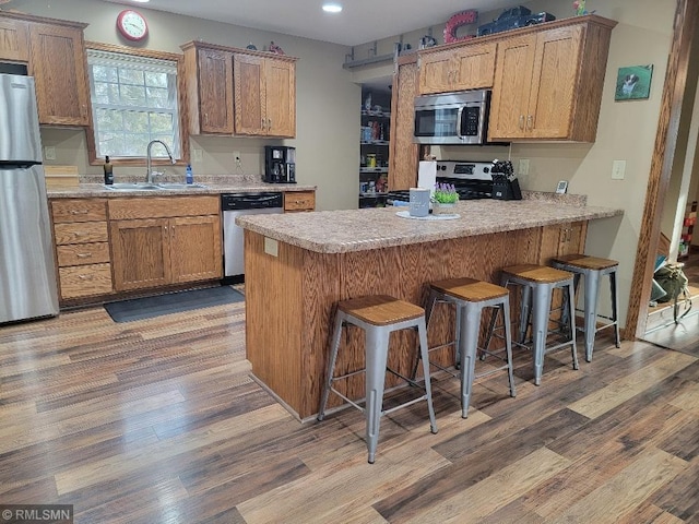 kitchen with light countertops, light wood-style flooring, appliances with stainless steel finishes, a peninsula, and a sink