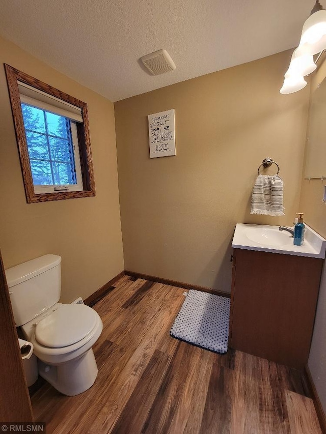 half bathroom with vanity, wood finished floors, baseboards, a textured ceiling, and toilet