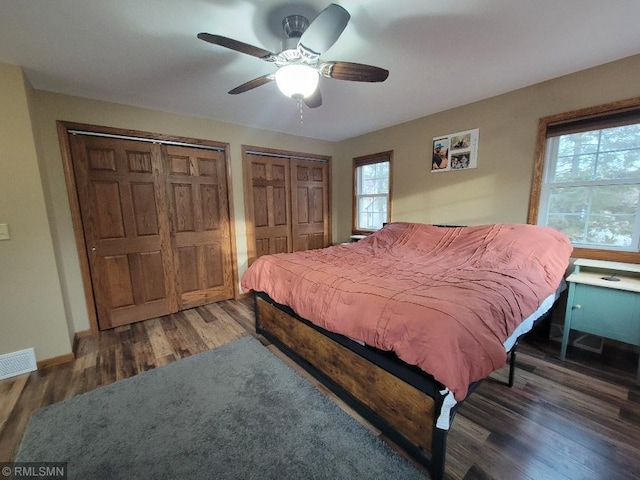 bedroom with visible vents, multiple closets, wood finished floors, baseboards, and ceiling fan