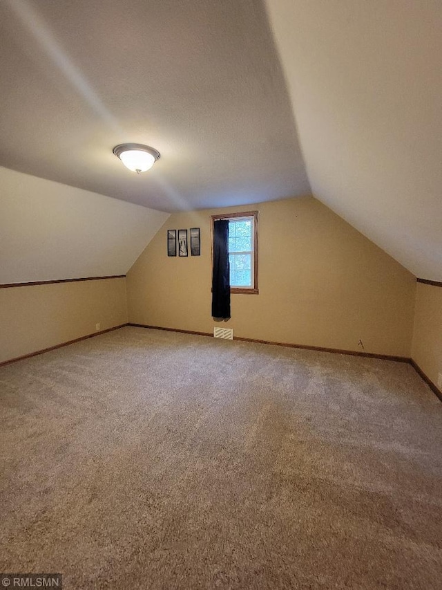 additional living space with vaulted ceiling, carpet flooring, baseboards, and visible vents