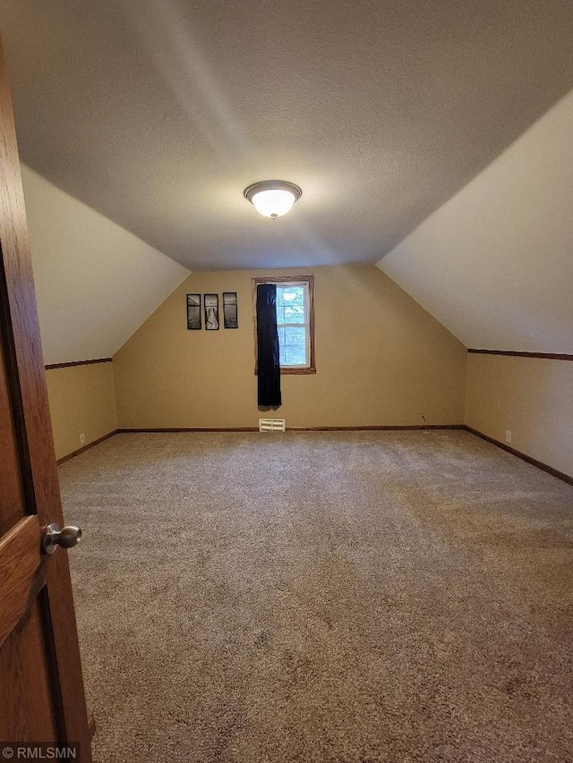 bonus room with vaulted ceiling, carpet flooring, baseboards, and a textured ceiling