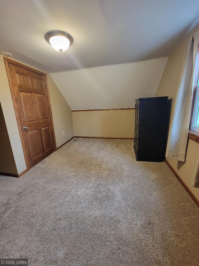 additional living space with lofted ceiling, light colored carpet, and baseboards