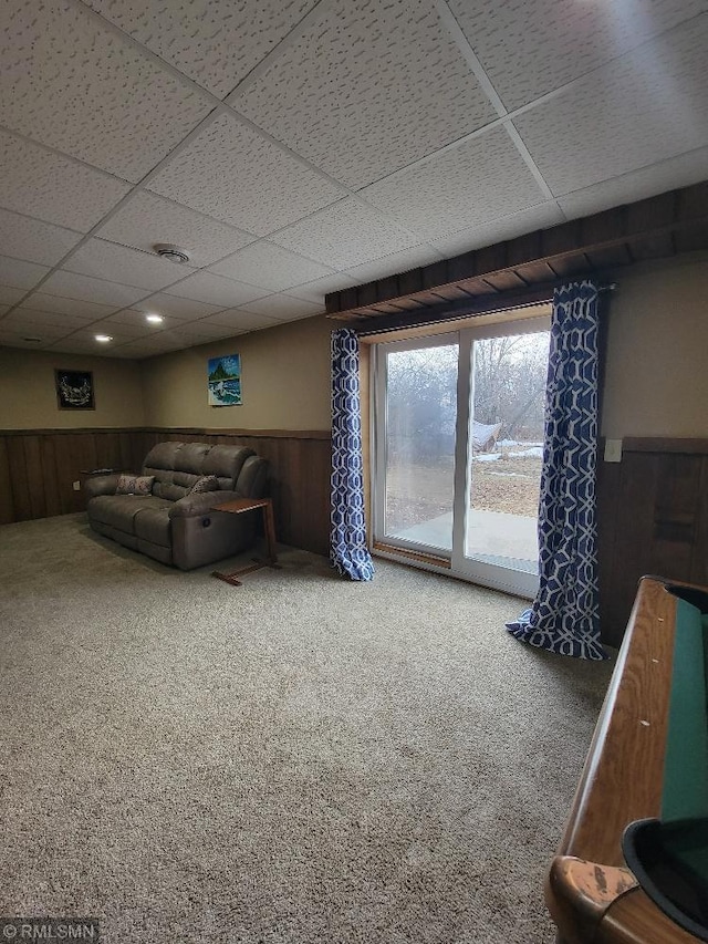 carpeted living area featuring a paneled ceiling, wood walls, and wainscoting