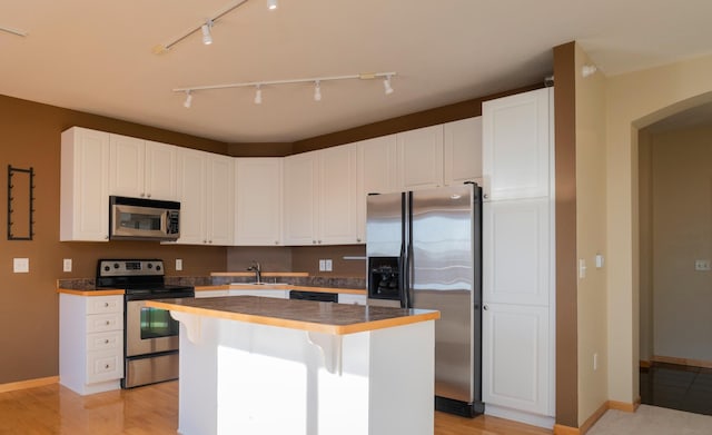 kitchen with a sink, a center island, white cabinetry, stainless steel appliances, and baseboards