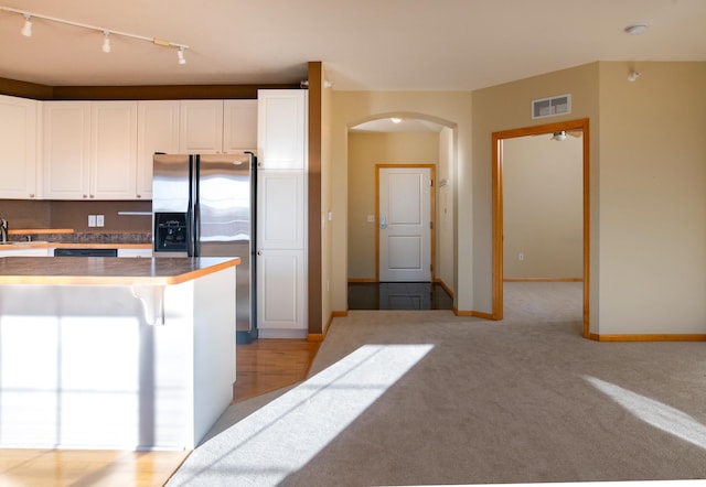 kitchen featuring visible vents, baseboards, arched walkways, stainless steel fridge, and white cabinetry