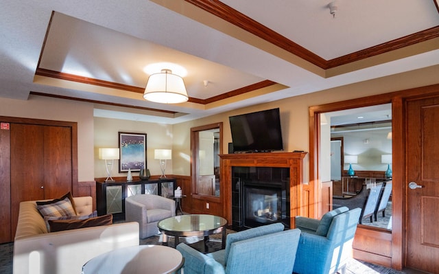 living room featuring a glass covered fireplace, wainscoting, a raised ceiling, and crown molding