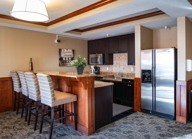 kitchen featuring a breakfast bar area, ornamental molding, a peninsula, stainless steel appliances, and a raised ceiling