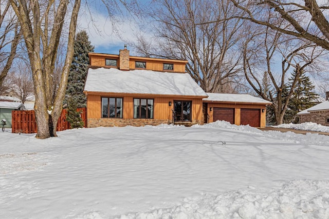 view of front of property with stone siding, an attached garage, a chimney, and fence