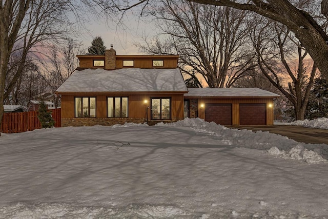 view of front of house featuring driveway, an attached garage, a chimney, and fence