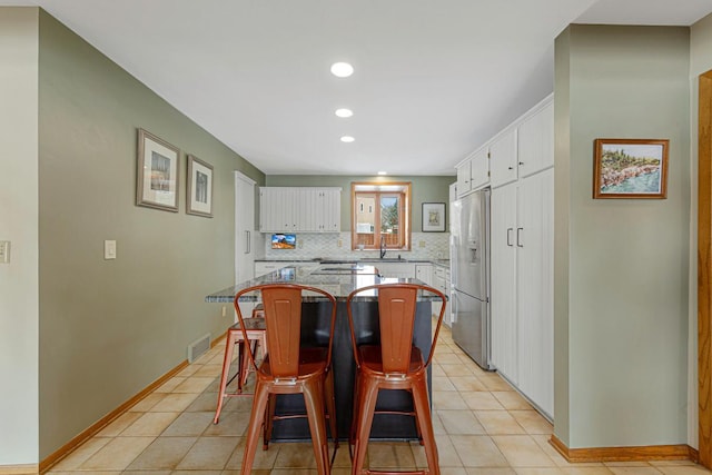 kitchen with decorative backsplash, white cabinets, visible vents, and stainless steel refrigerator