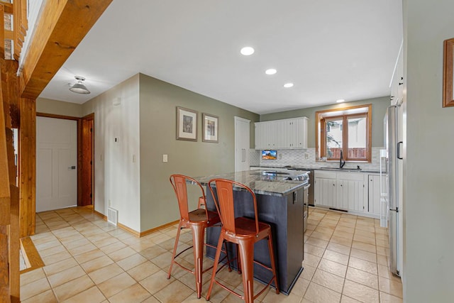 kitchen with a sink, white cabinets, a kitchen bar, tasteful backsplash, and a center island