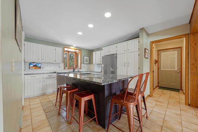 kitchen featuring a breakfast bar area, stainless steel fridge with ice dispenser, a sink, decorative backsplash, and white cabinets