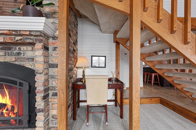 carpeted office space with wooden walls and a lit fireplace