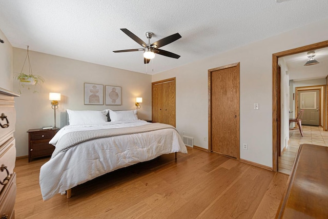 bedroom featuring two closets, visible vents, light wood-style floors, and a textured ceiling