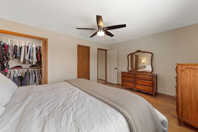 bedroom featuring a textured ceiling, a closet, light wood-style floors, baseboards, and ceiling fan