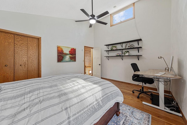 bedroom featuring ceiling fan, baseboards, wood finished floors, and a towering ceiling