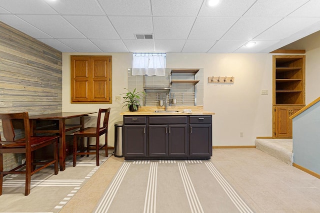 bar featuring wooden walls, baseboards, visible vents, a drop ceiling, and a sink