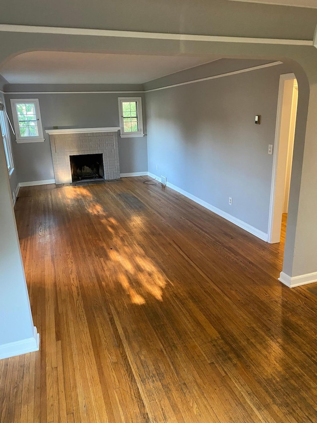 unfurnished living room featuring baseboards, hardwood / wood-style floors, a fireplace, arched walkways, and plenty of natural light