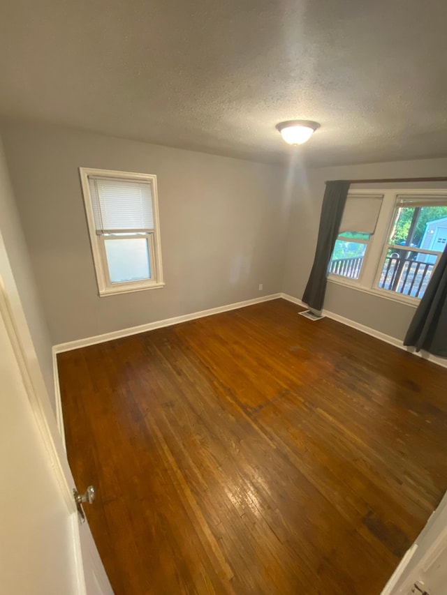 unfurnished room featuring visible vents, baseboards, a textured ceiling, and dark wood-style floors